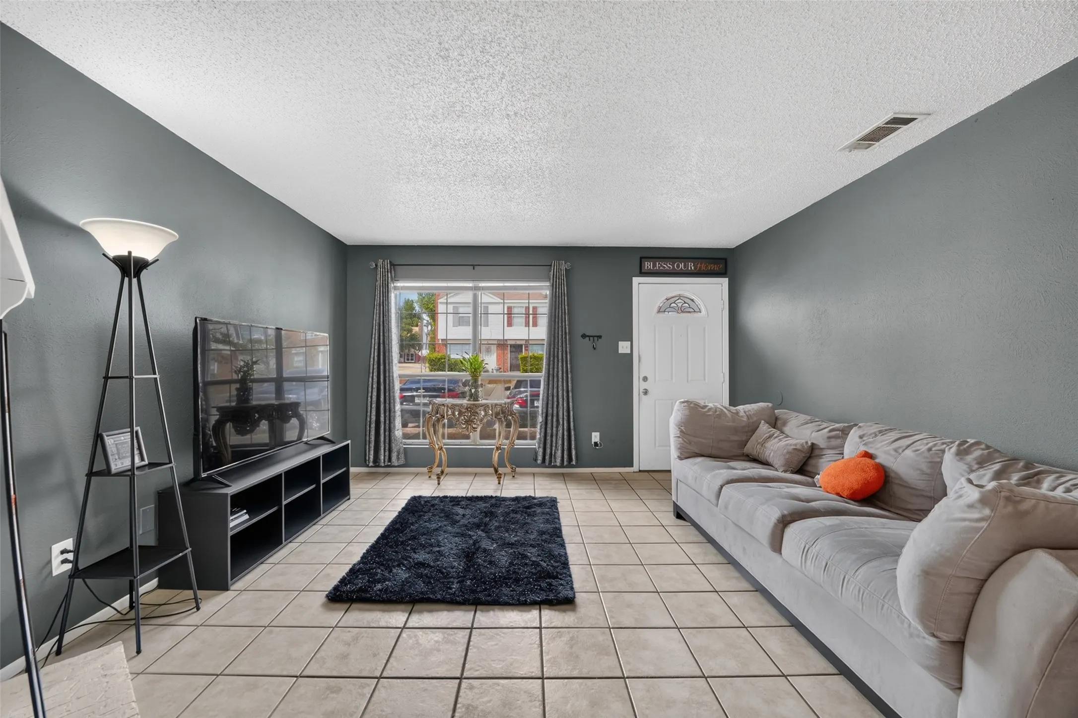 Spacious living area featuring tile flooring, a large window with drapes, and a white paneled entry door