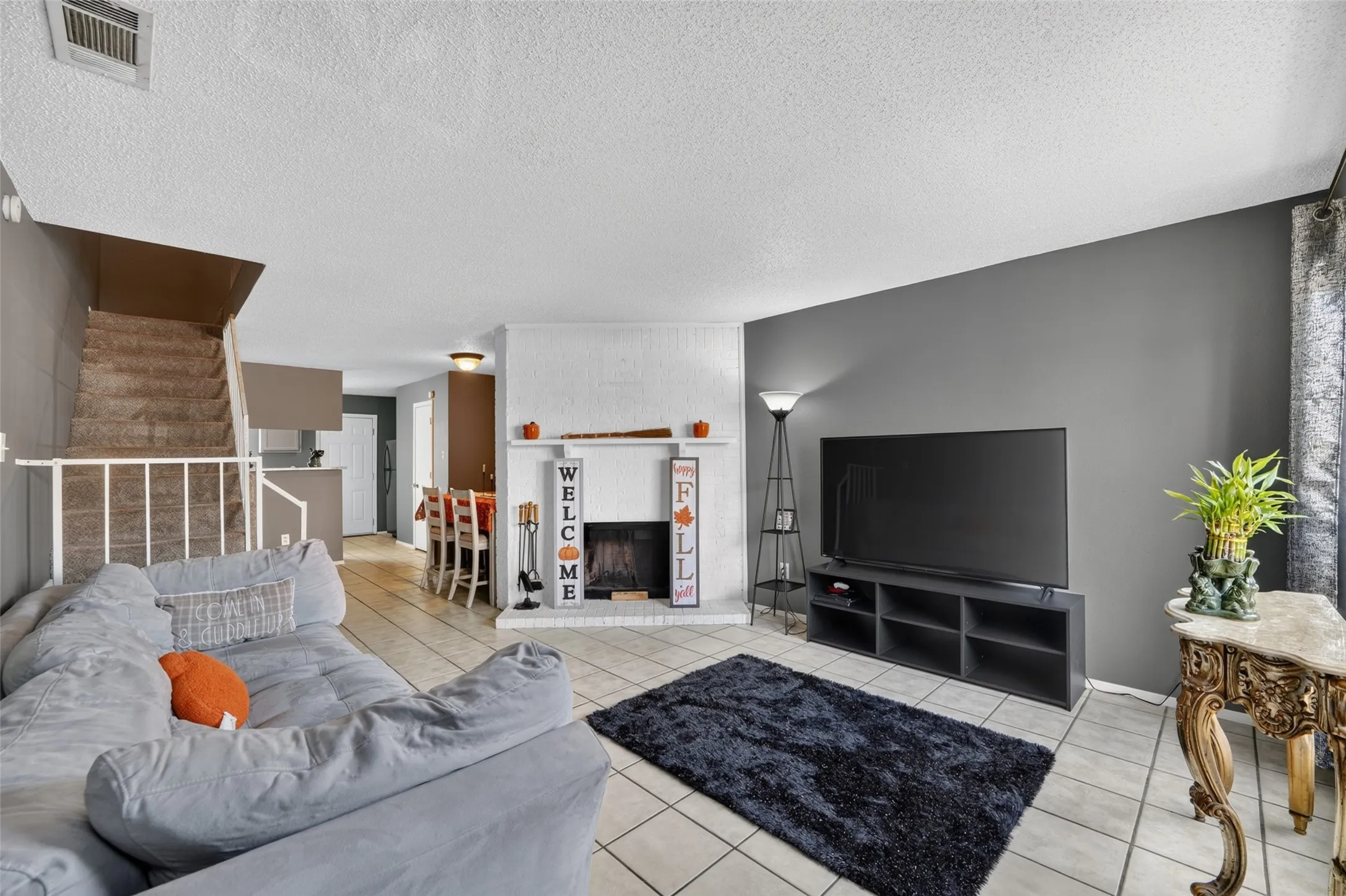 Tiled flooring, white brick fireplace, painted accent wall, carpeted staircase, and built-in shelving