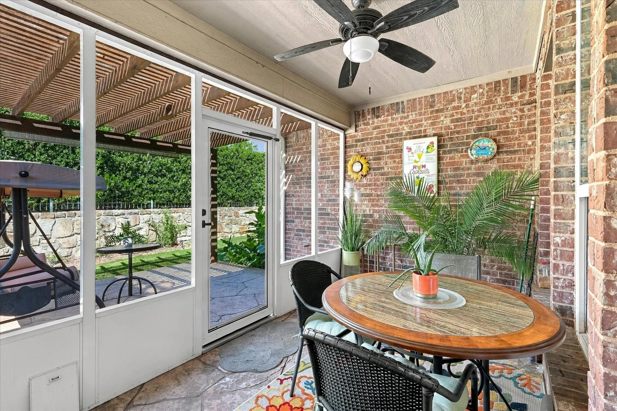 Enclosed patio featuring a brick accent wall, stone-patterned flooring, and a ceiling fan