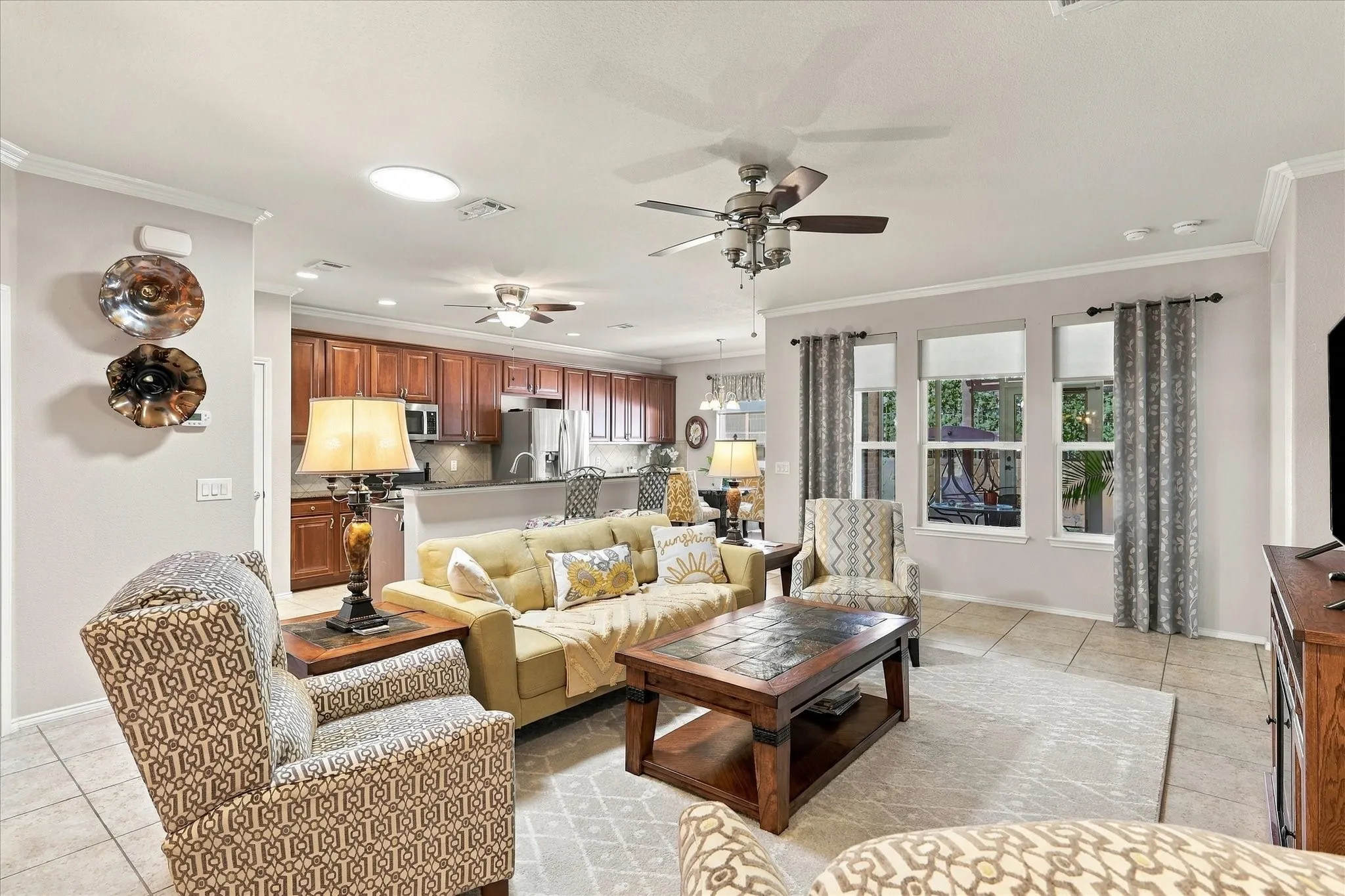 Open-concept living space featuring tile flooring, crown molding, a built-in ceiling fan, and multiple windows