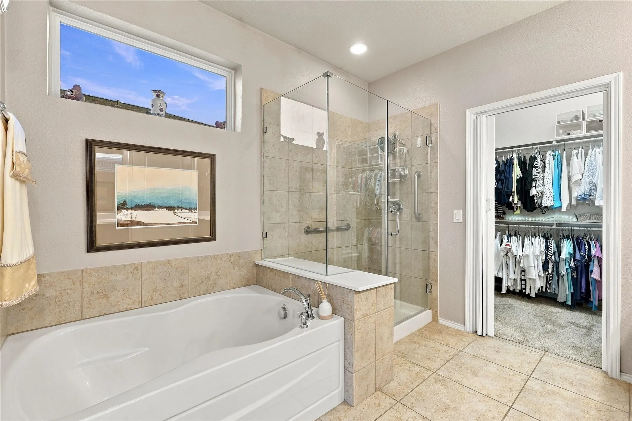 Soaking tub with tile surround, glass-enclosed shower, tiled flooring, and a walk-in closet with built-in shelving