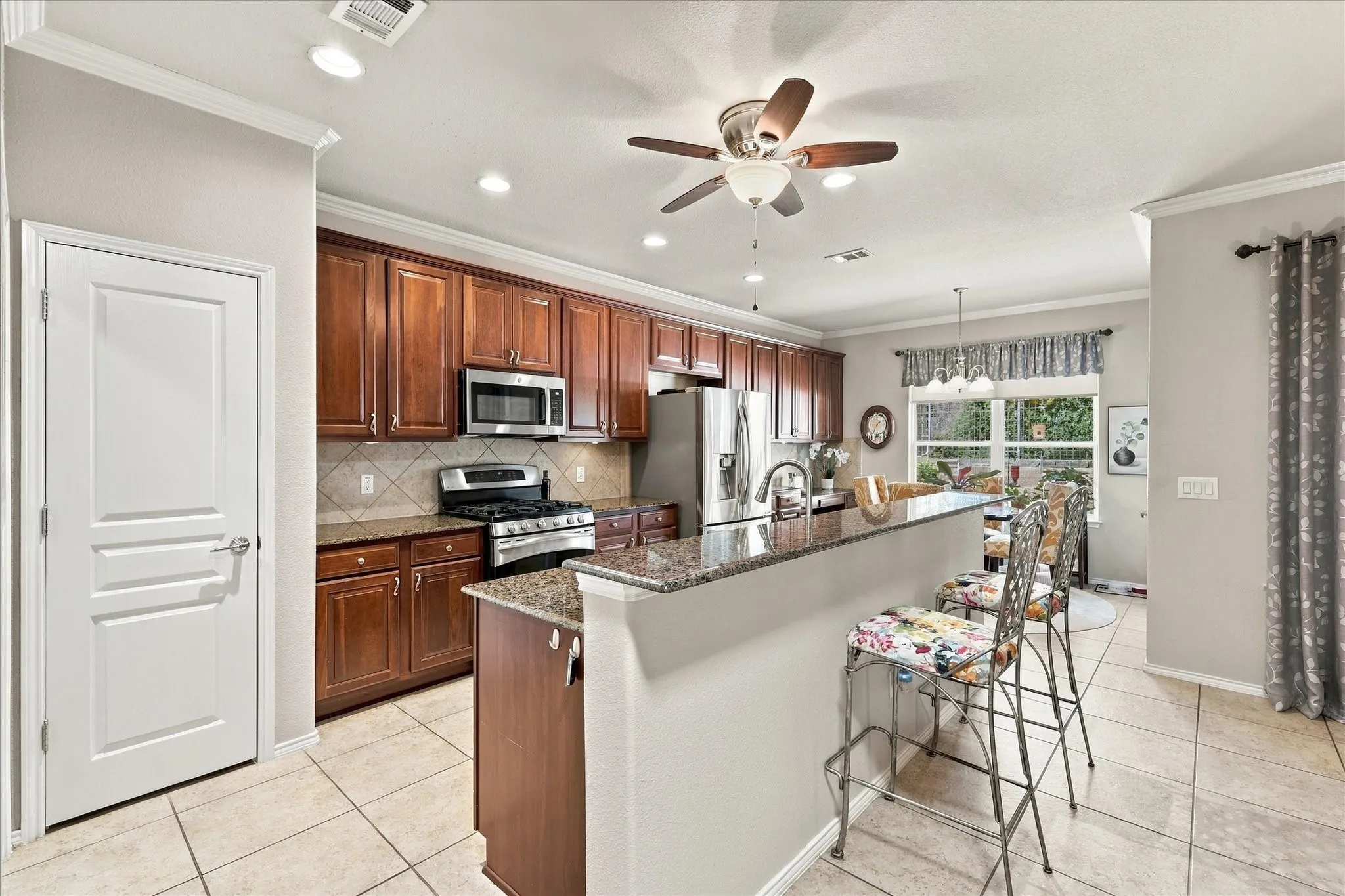 Kitchen featuring wood cabinetry, stainless steel appliances, a breakfast bar with granite countertops, tiled flooring, and recessed lighting