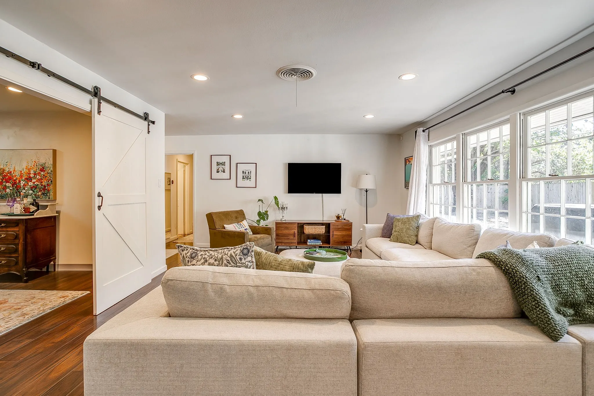 Spacious open-concept living area featuring a large sectional seating arrangement, hardwood flooring, recessed ceiling lighting, and abundant natural light from multi-pane glass doors and windows