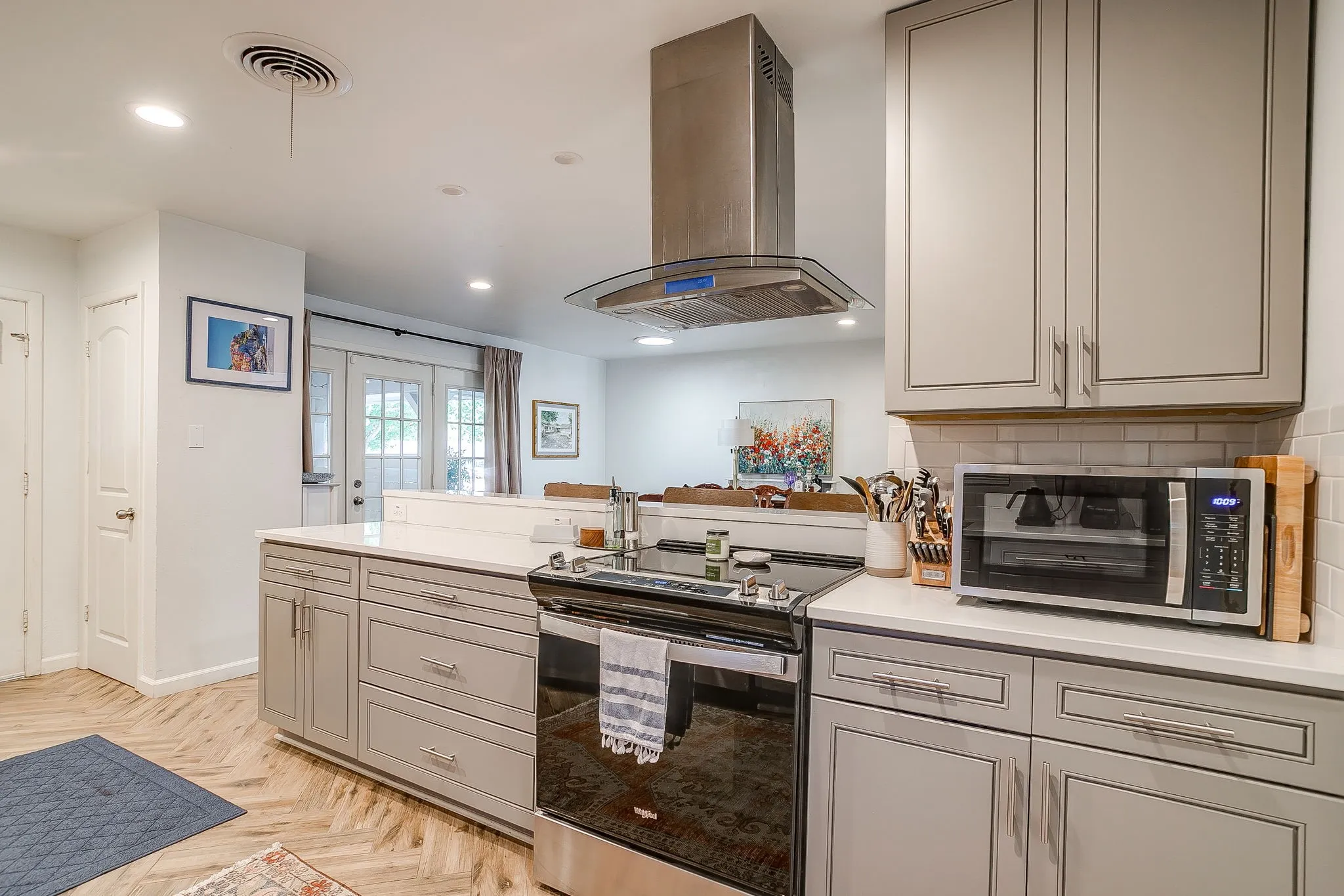 Kitchen featuring light gray cabinetry, stainless steel range and hood, white subway tile backsplash, and light-toned countertops
