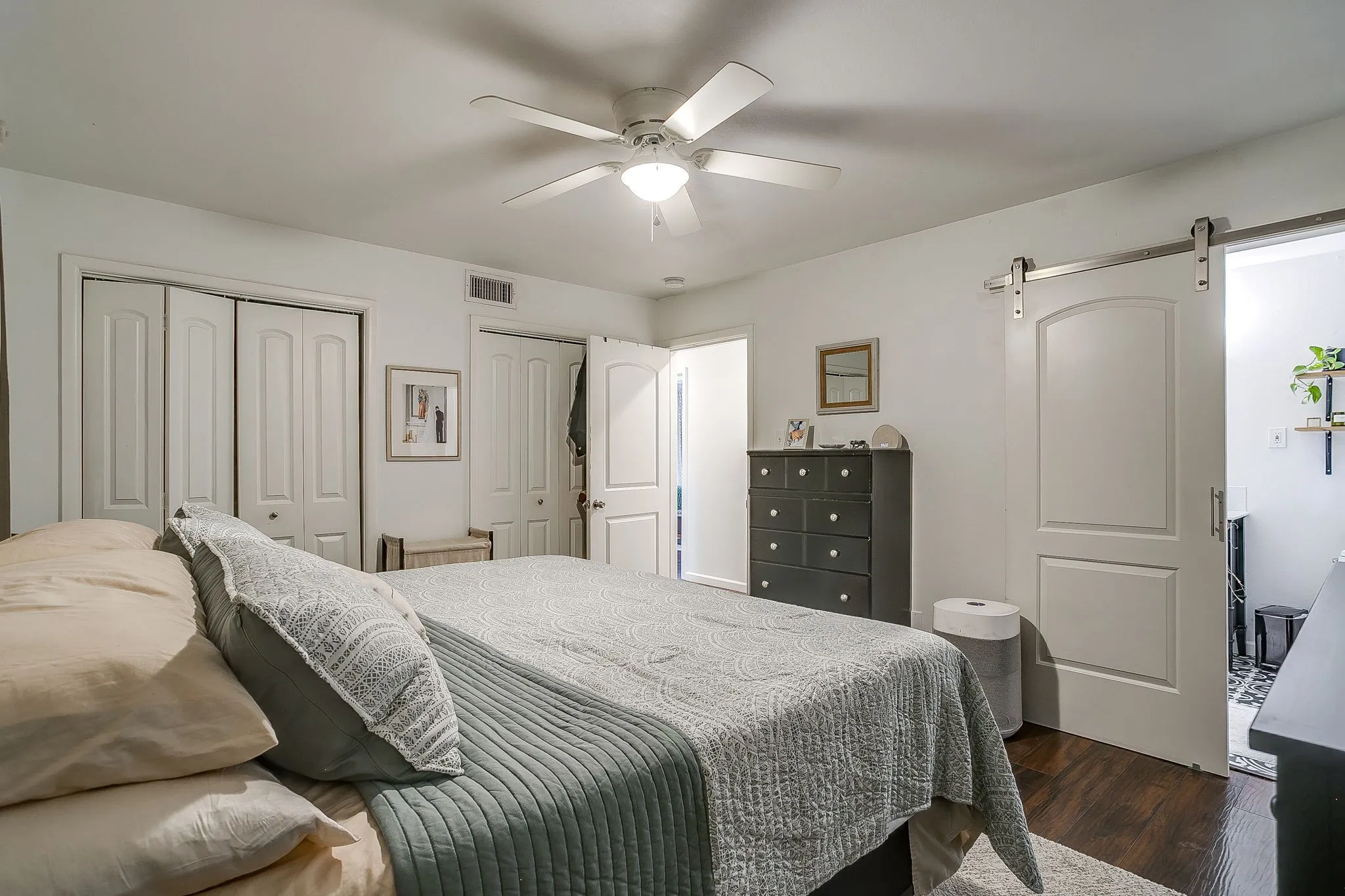 Ceiling fan with integrated lighting, wood-finish flooring, white bi-fold closet doors, white interior doors, and a barn door entry