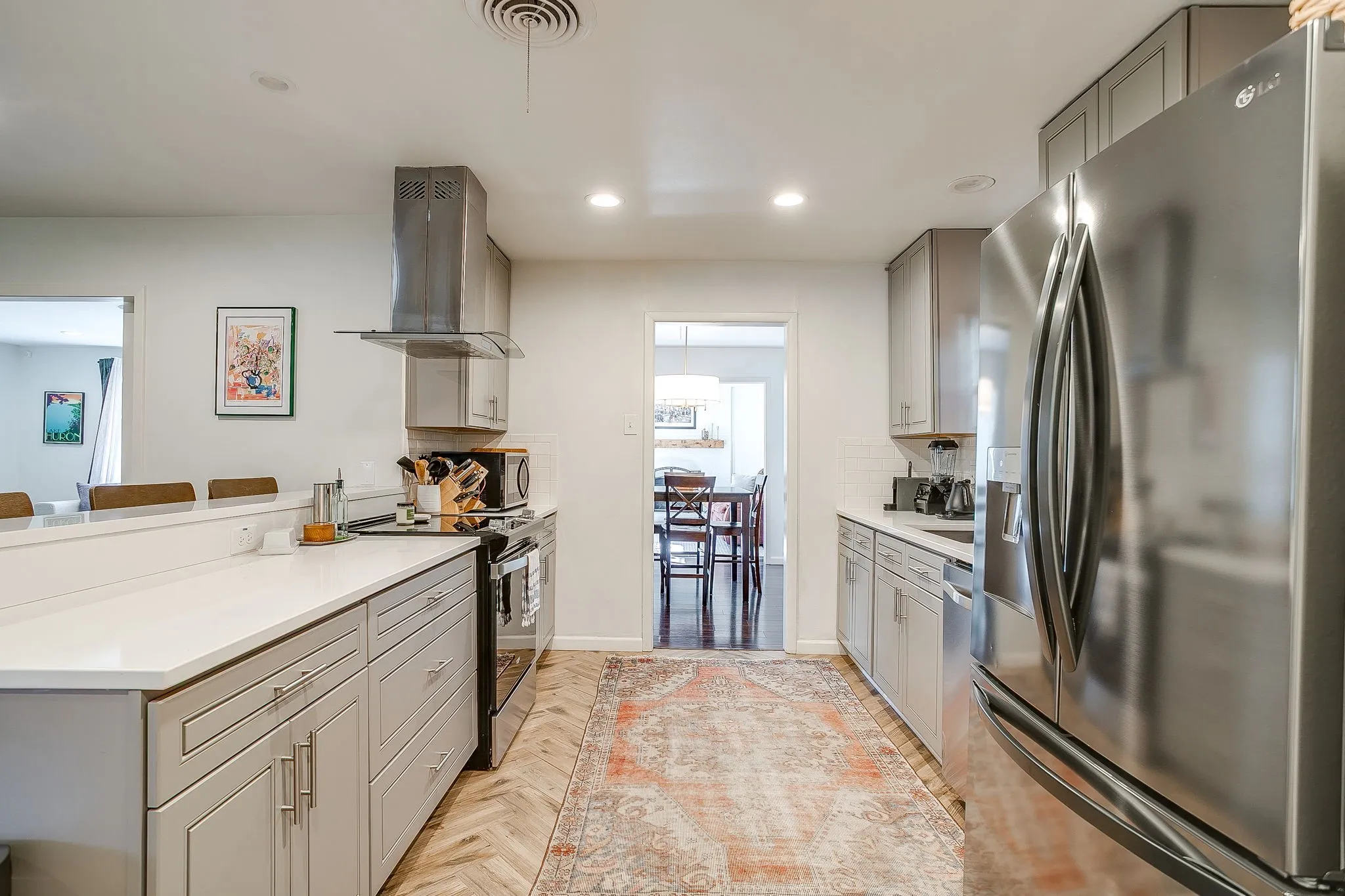 Recessed lighting illuminating a kitchen featuring stainless steel appliances, a range hood, and light-colored cabinetry with modern hardware