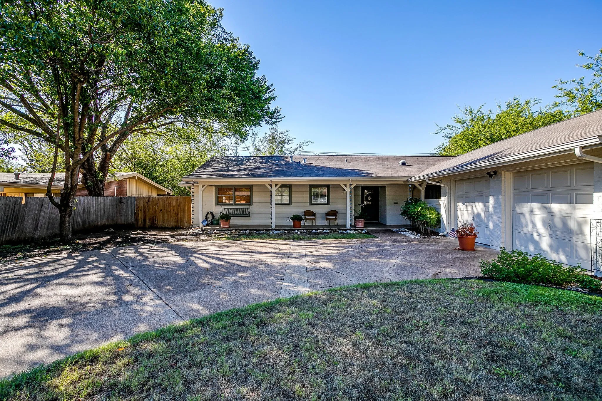 Charming single-story home with a spacious concrete patio, mature shade trees providing natural coverage, and manicured lawn