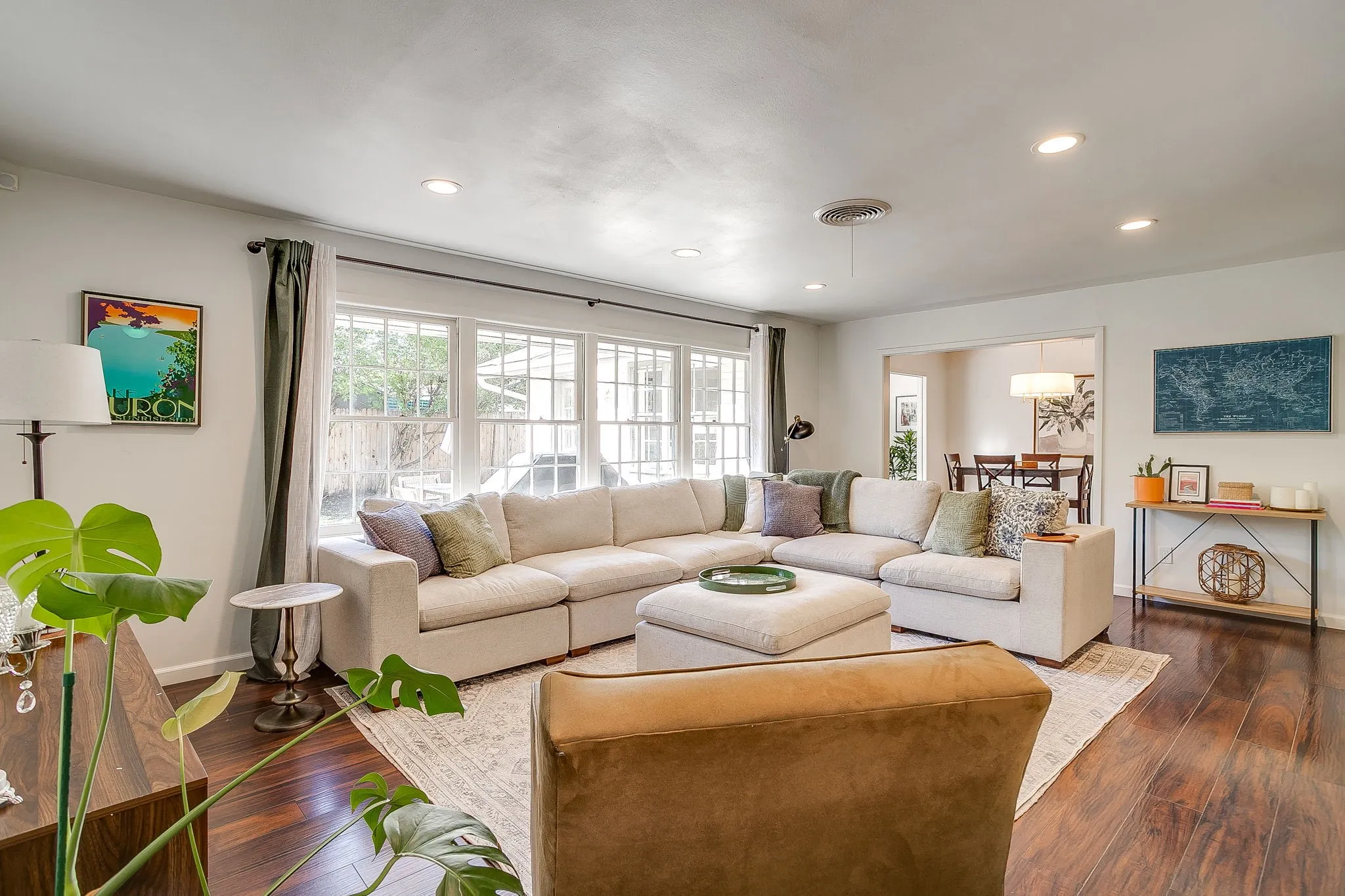 Recessed lighting, dark wood-finish flooring, white walls, large multi-pane windows, and a doorway opening to an additional room