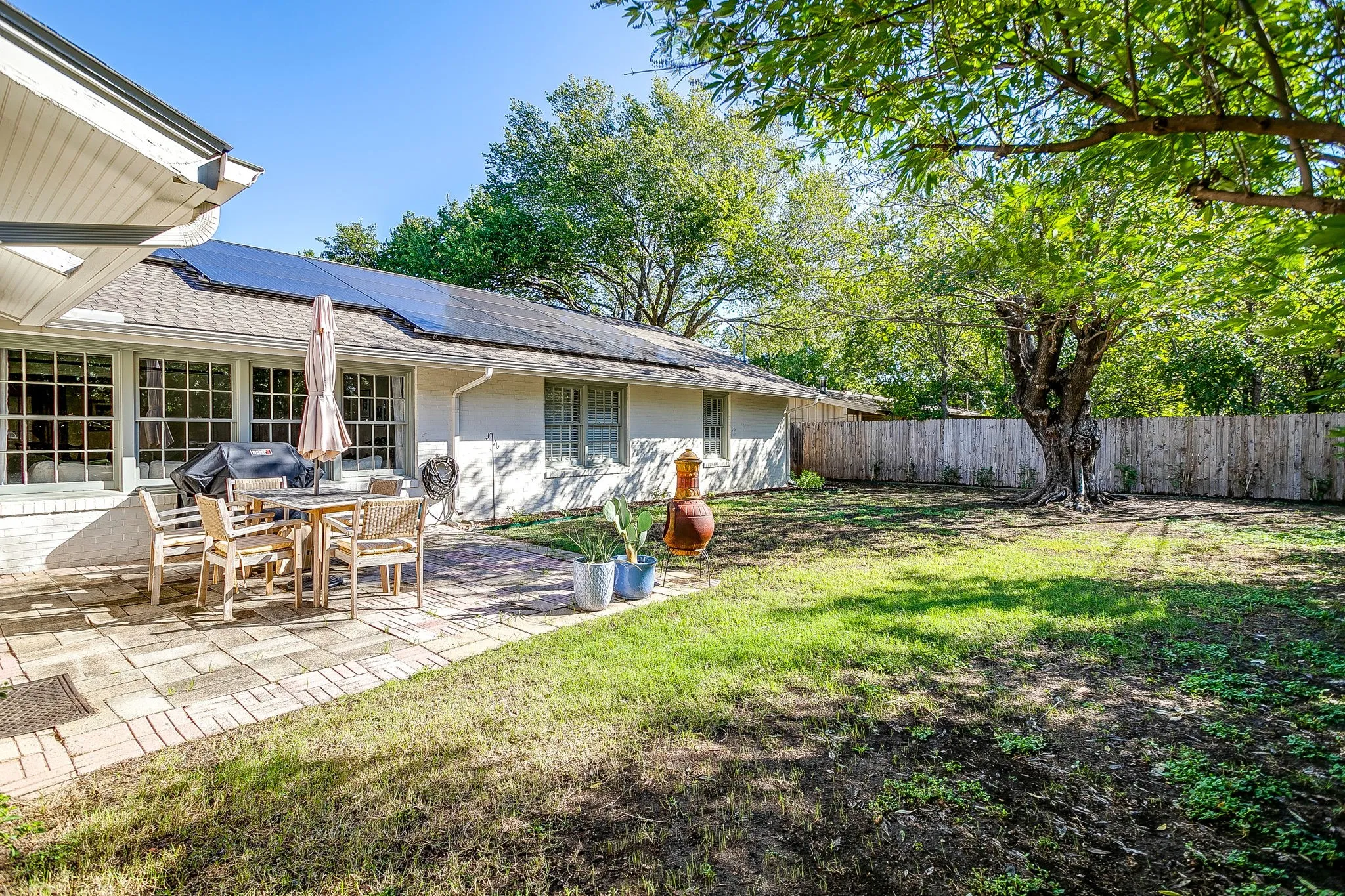 Patio with paver flooring, extensive back lawn, mature trees, and solar panels installed on the roof