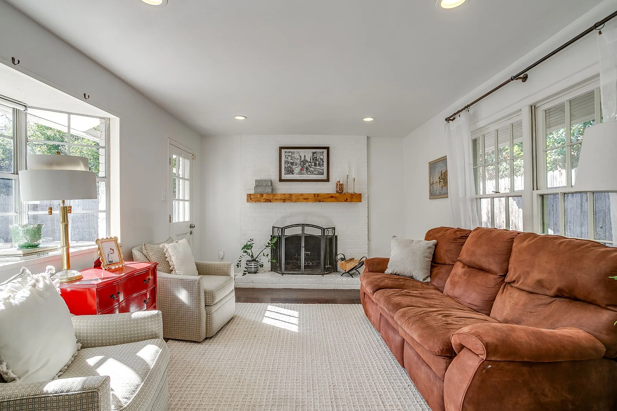 Bright, open living space featuring a wood-burning fireplace with decorative mantel, recessed ceiling lighting, and abundant natural light from multiple windows and glass doors