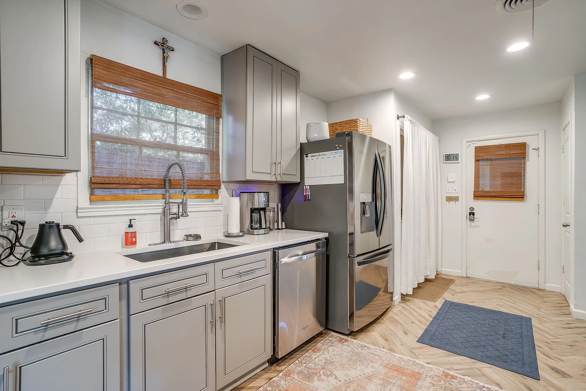 Gray shaker-style cabinetry with chrome hardware, white subway tile backsplash, stainless steel appliances, and light wood-finish flooring