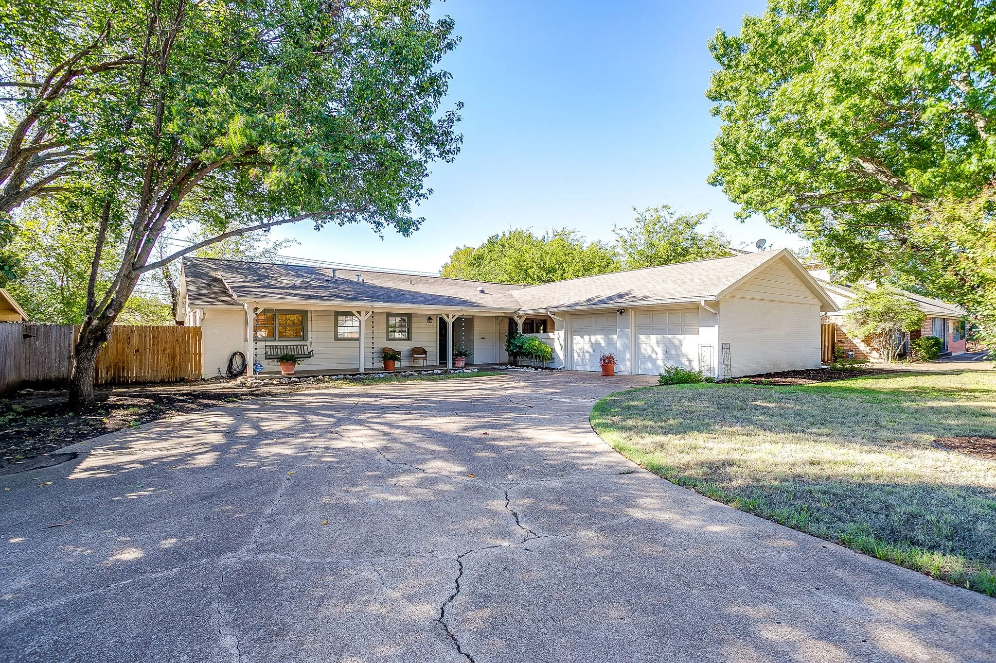 Ranch-style exterior with a covered porch, attached garage, mature trees, and a concrete driveway