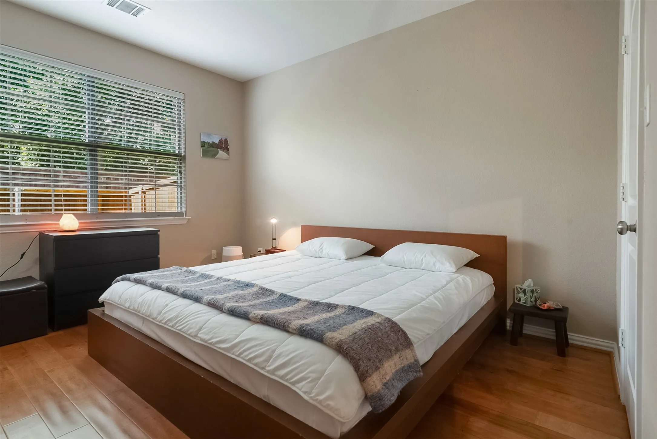 Warm wood-finish flooring with a neutral wall color and natural light from a window with horizontal blinds