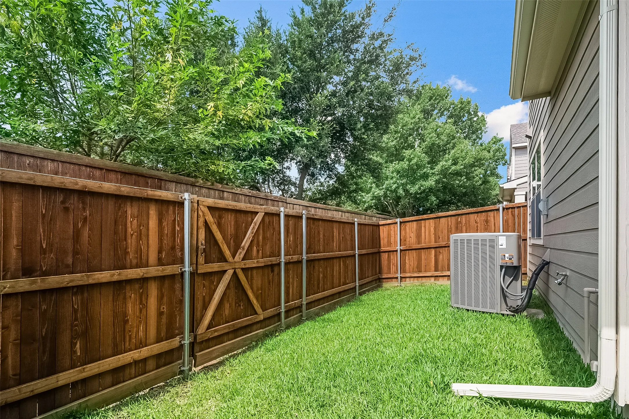Enclosed backyard featuring a wood privacy fence, a gate with cross bracing, and a well-maintained lawn