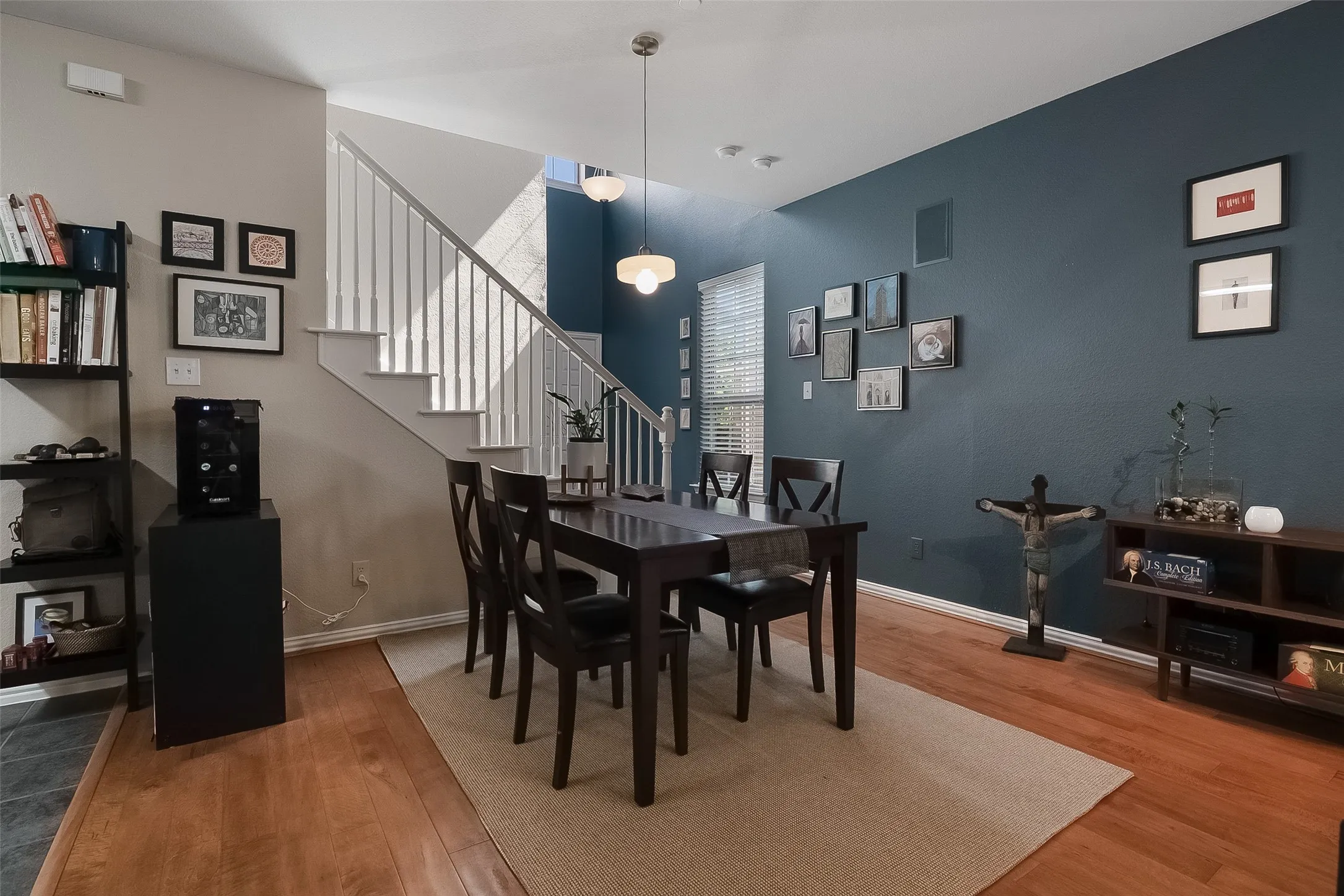 Hardwood flooring, painted accent wall, window with blinds, and staircase with balusters