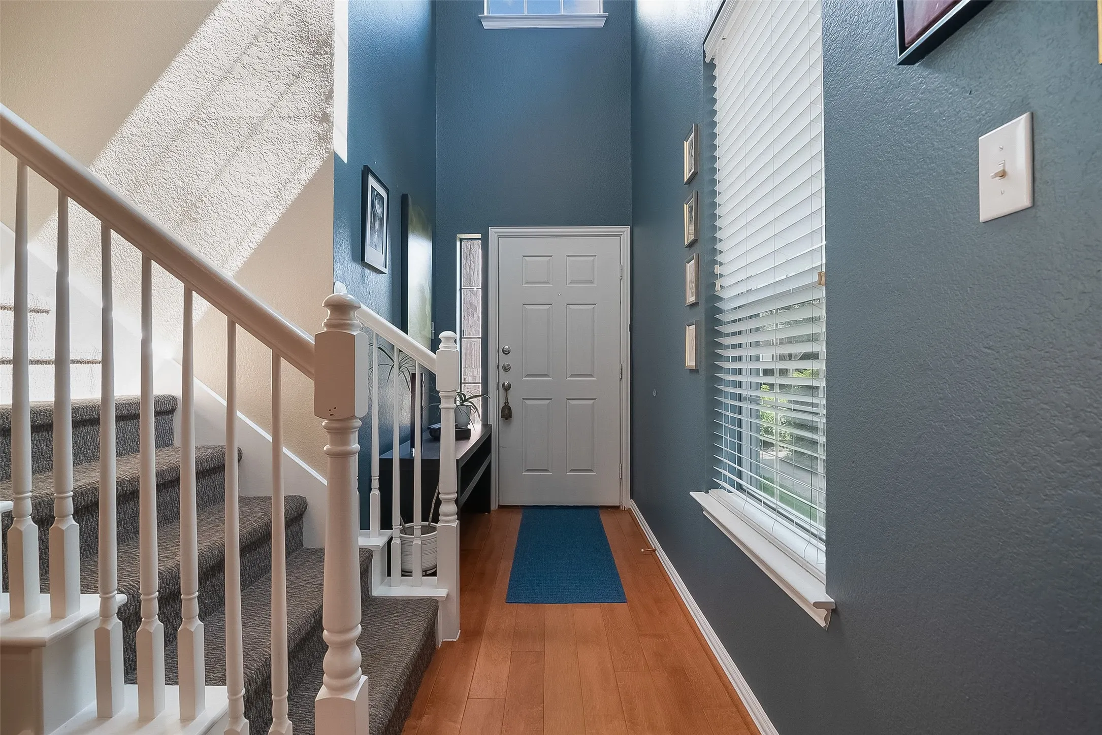 Entryway featuring wood-finish flooring, a white paneled door, and a staircase with white balusters and carpeted treads