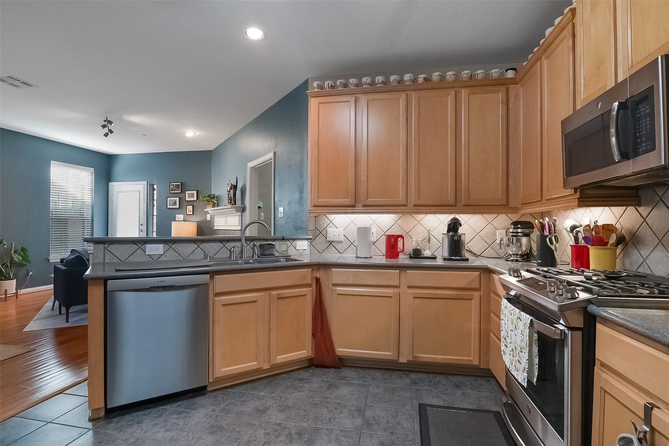 Kitchen featuring wood cabinetry, stainless steel appliances, tile backsplash, and dark countertops