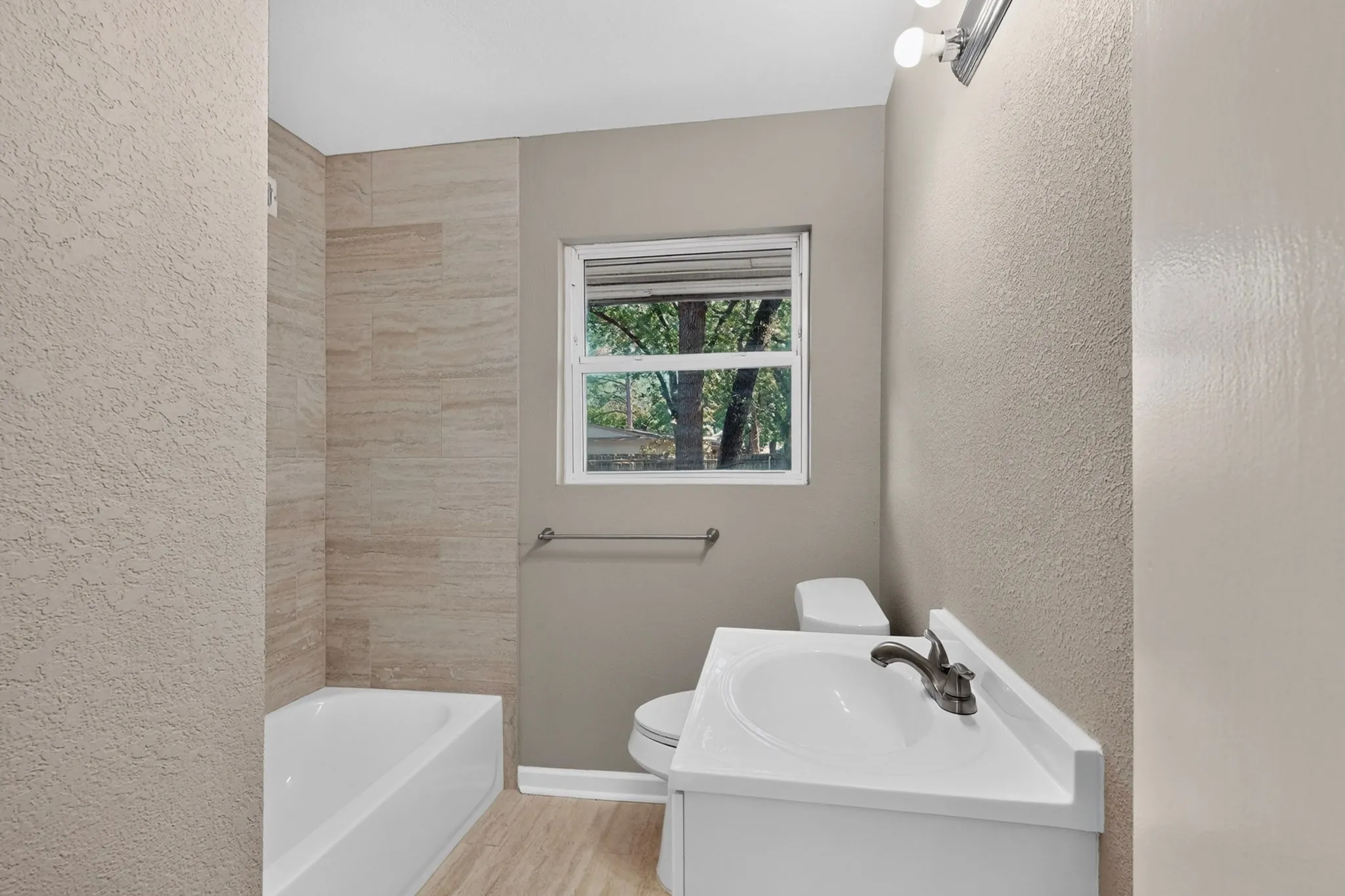 Bathroom featuring a white vanity with integrated sink, a toilet, a window, and a bathtub with tiled surround
