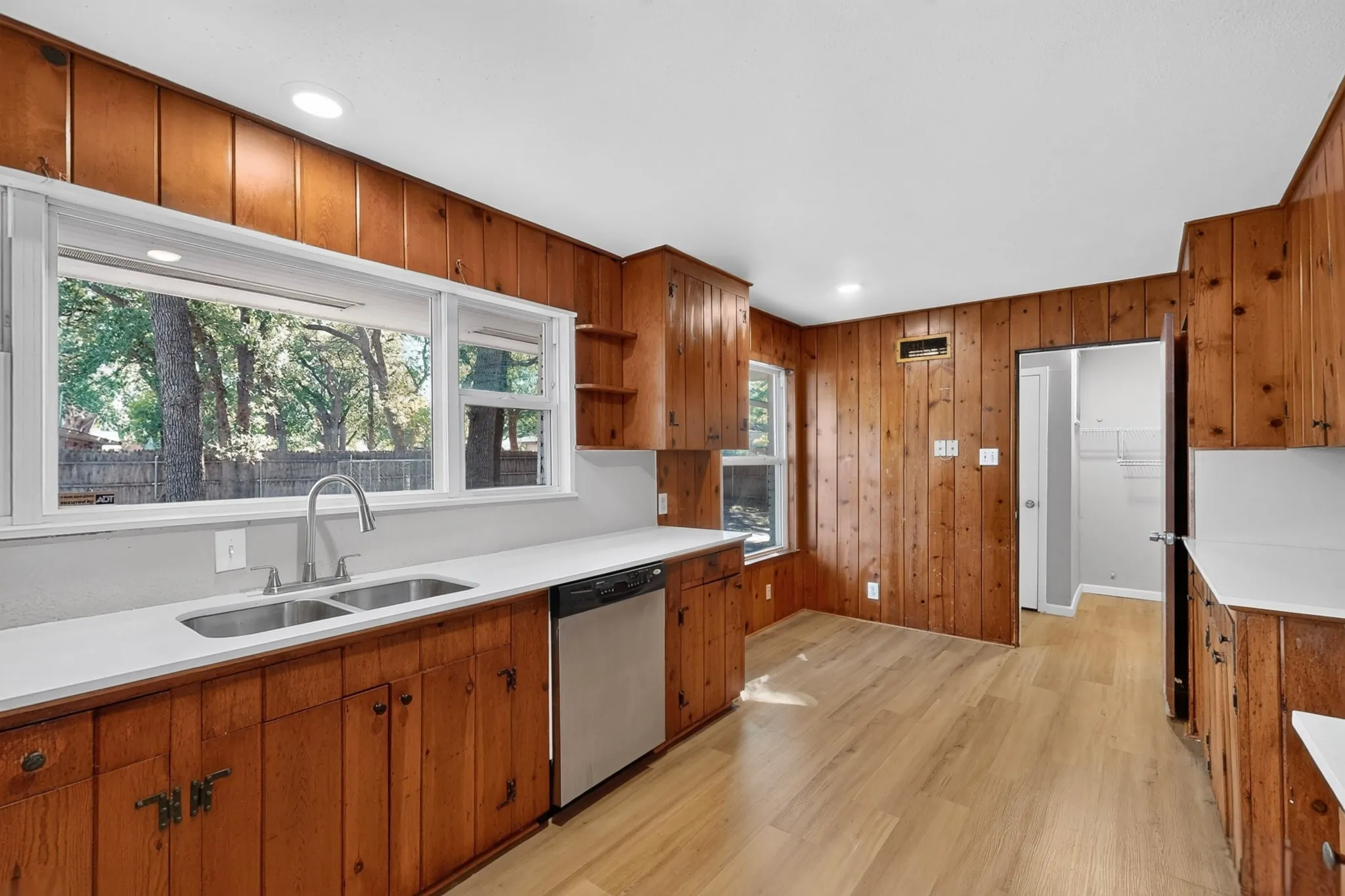 Kitchen featuring wood-paneled walls, wood-finish flooring, white countertops, and a dual basin stainless steel sink with a gooseneck faucet