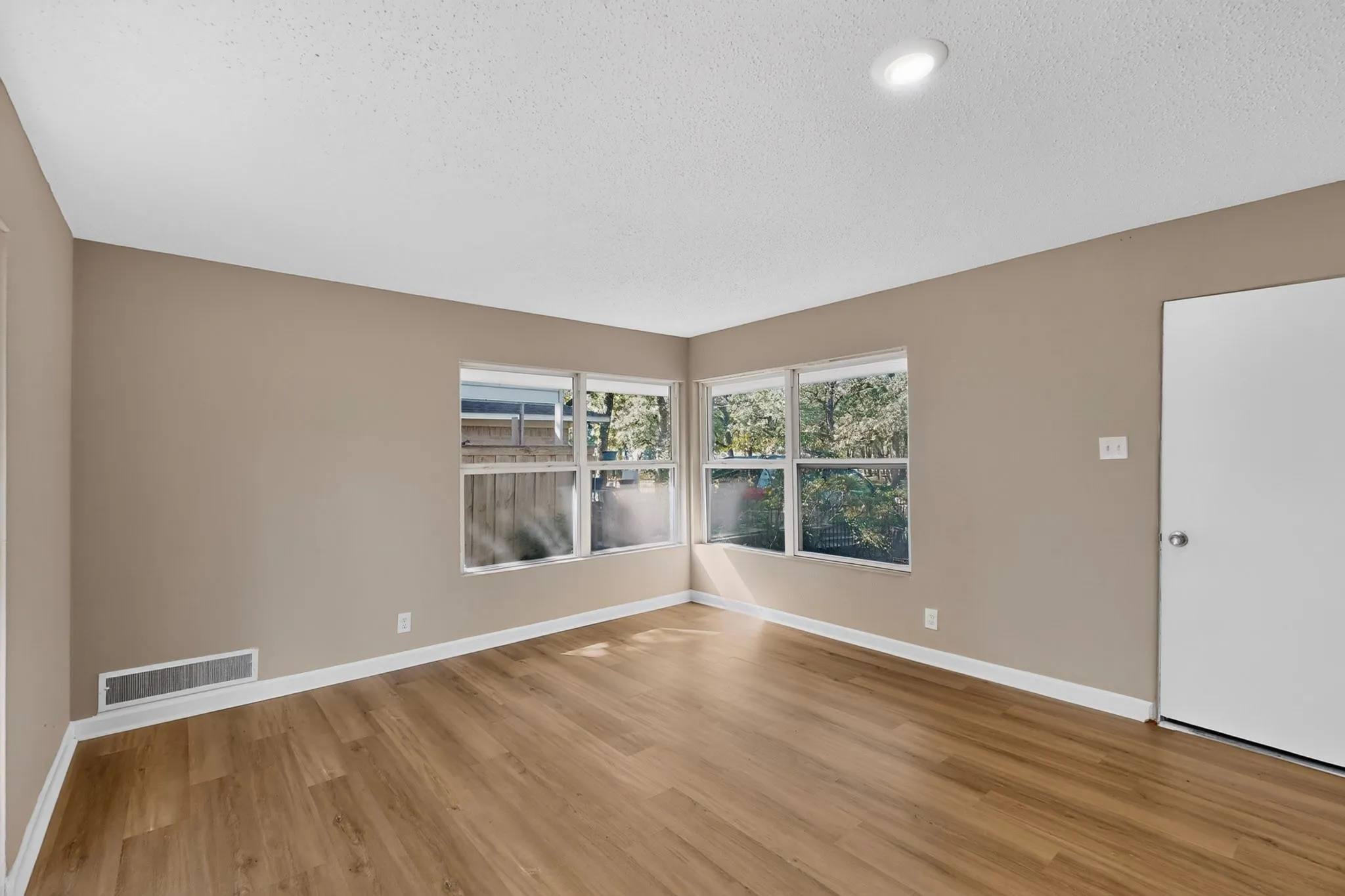 Wood-finish flooring throughout, multiple windows, recessed ceiling lighting, neutral wall tones, and white trim