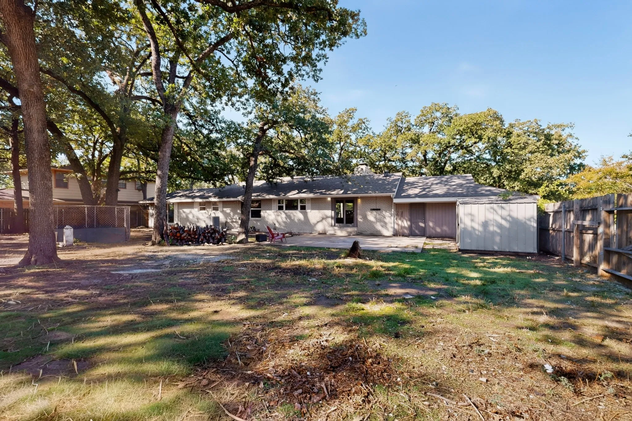 Expansive rear yard with mature trees, a concrete patio, and a utility shed