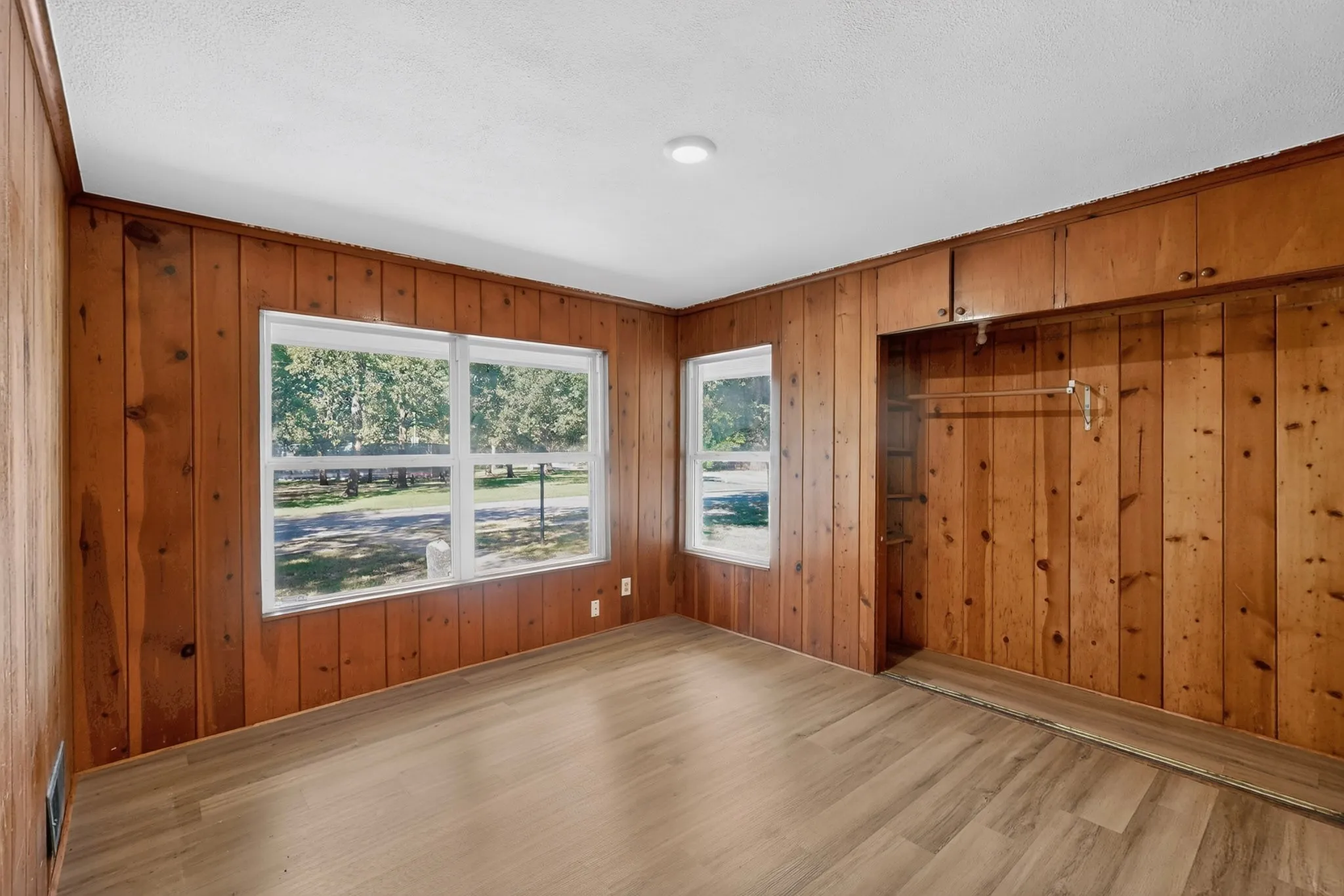 Wood-finish flooring, wood panel walls, recessed lighting, multiple windows, and built-in closet storage