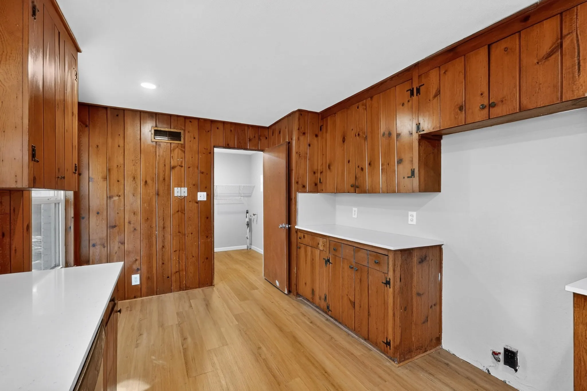 Wood-paneled walls and cabinetry, white countertops, wood-finish flooring, and recessed lighting