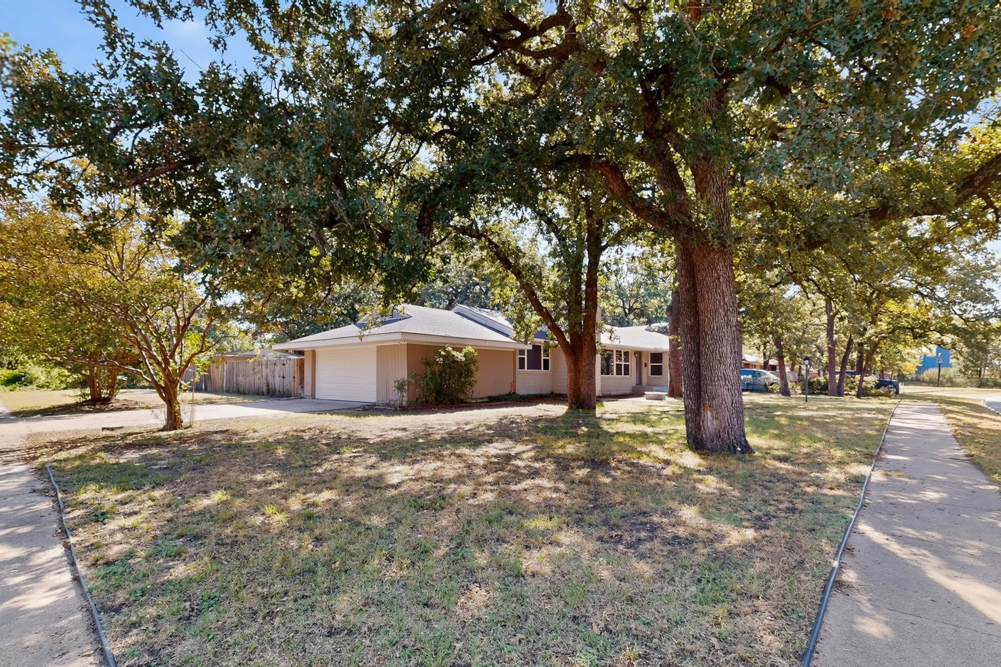 Single-story residence featuring a two-car garage, mature shade trees, and a concrete pathway