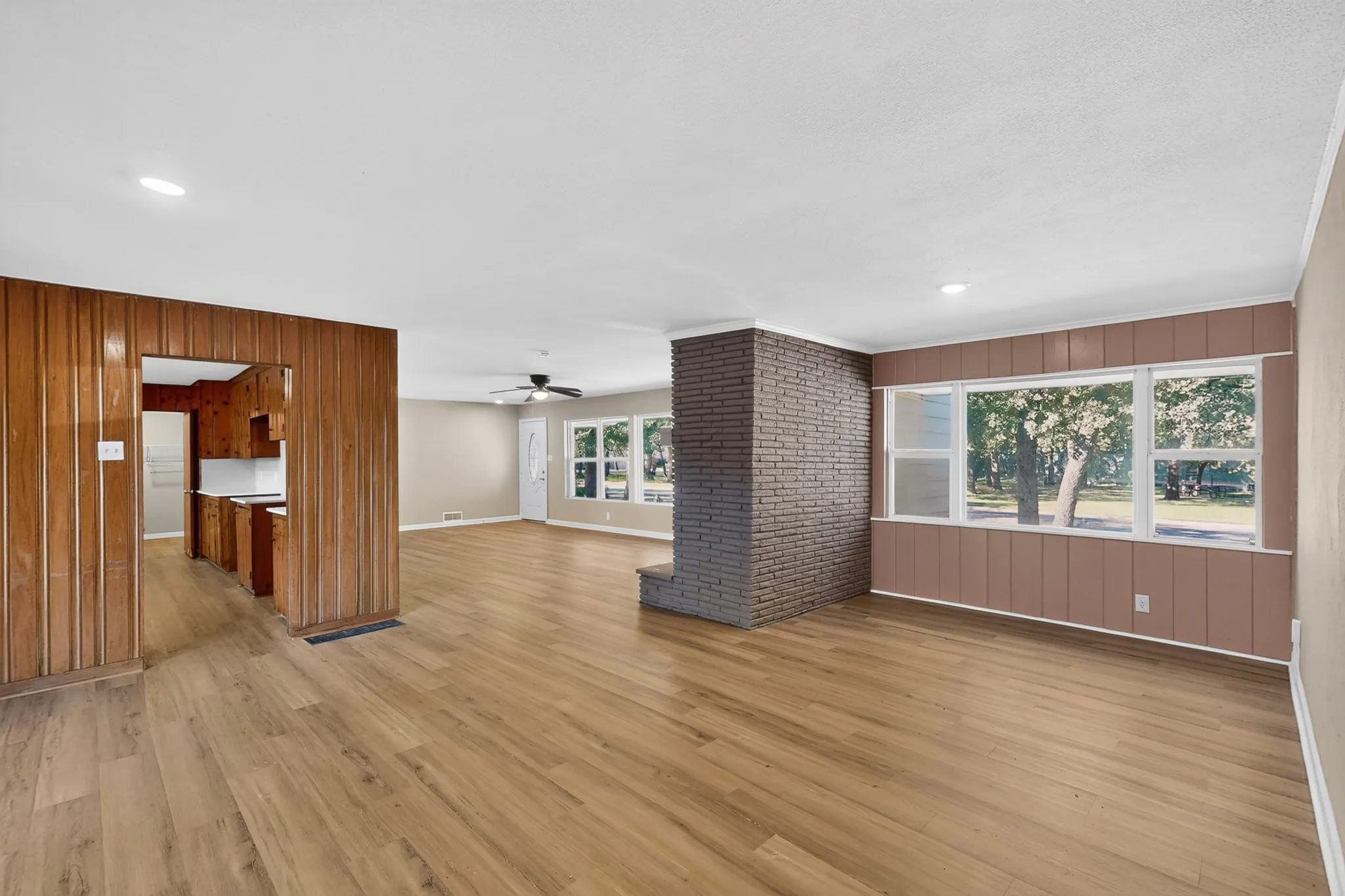 Open-concept living space with wood-finish flooring, a brick accent wall, and multiple windows