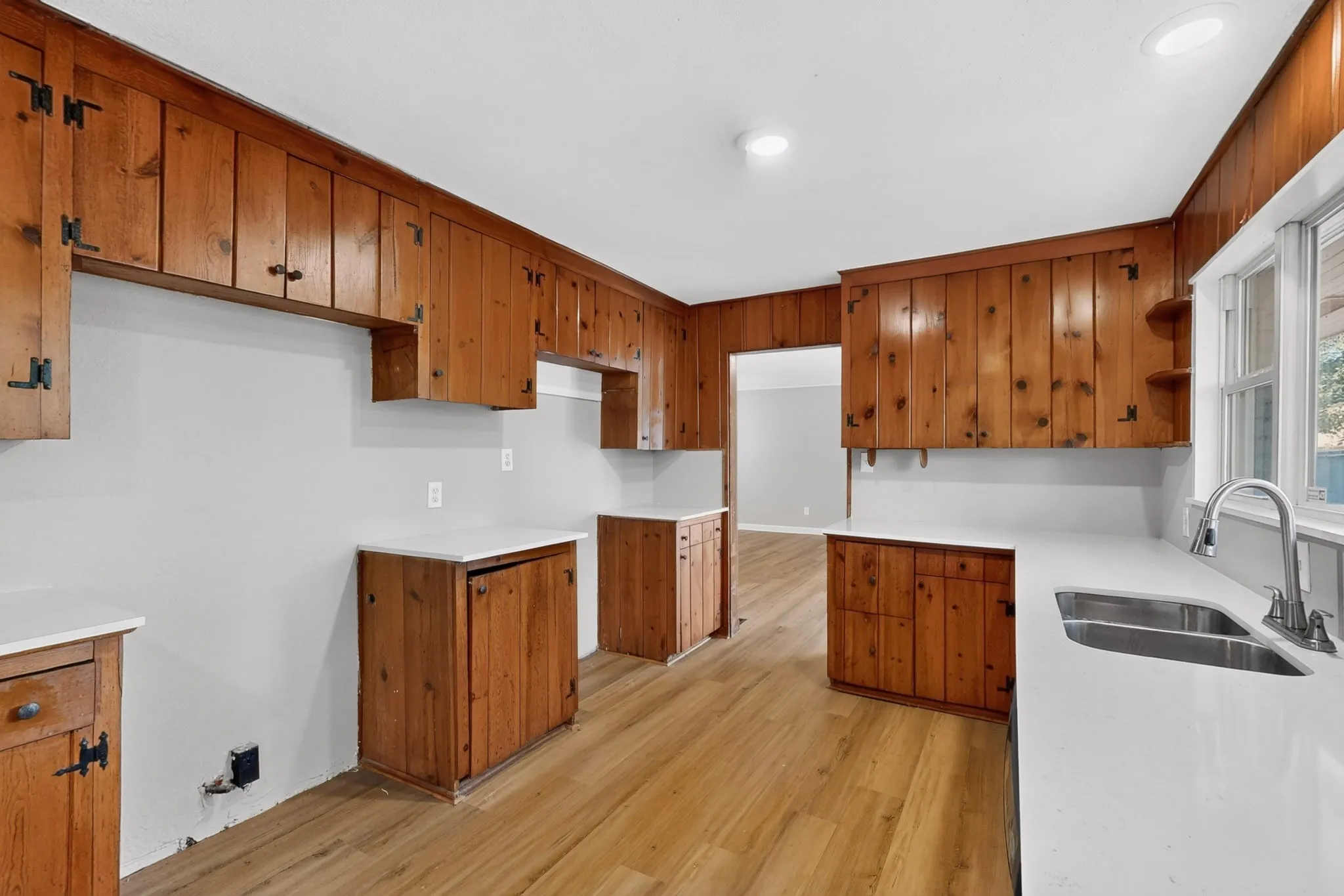 Kitchen featuring extensive wood cabinetry, wood-finish flooring, recessed lighting, white countertops, and a double basin stainless steel sink with a pull-down faucet