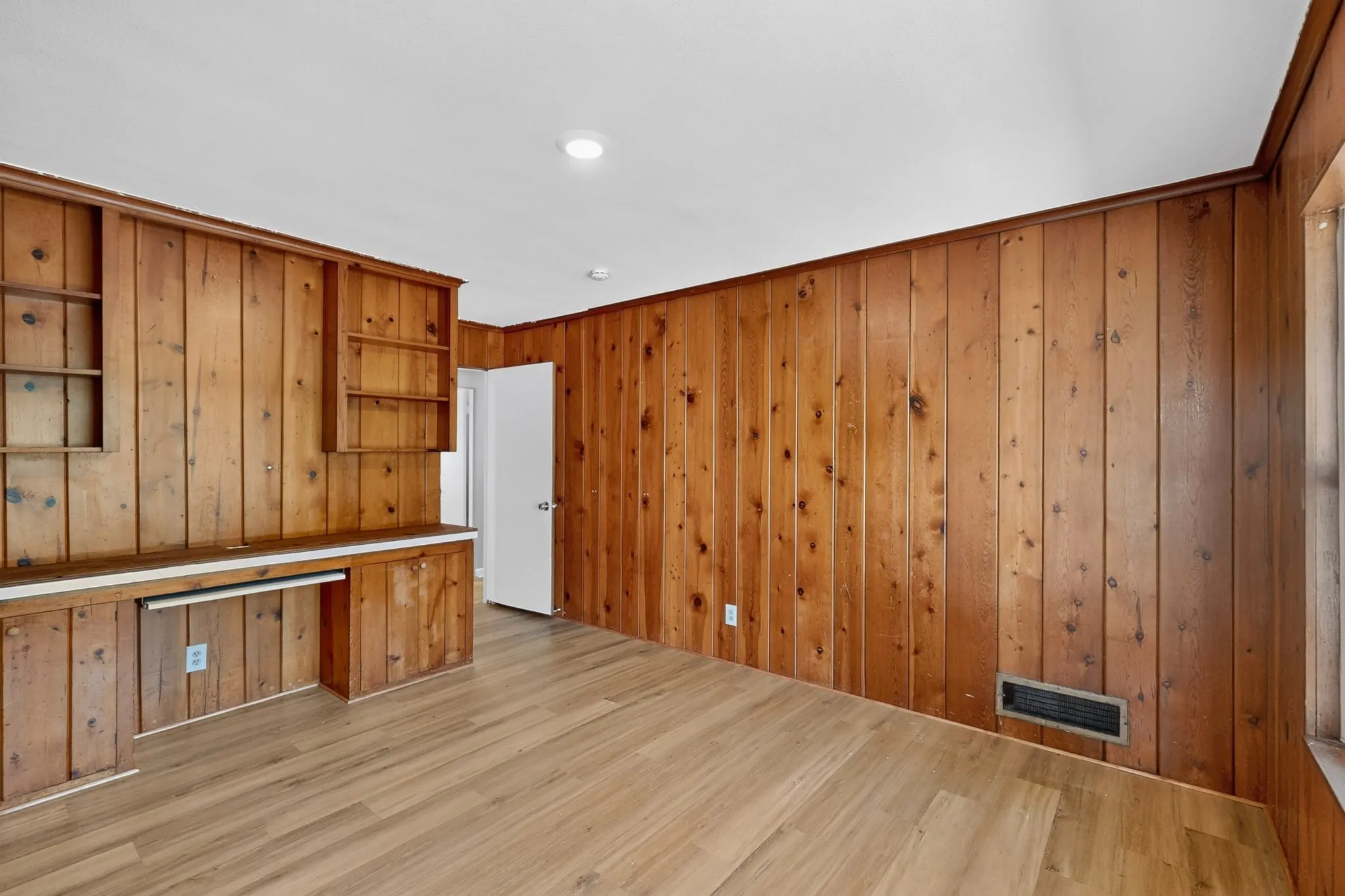 Wood-paneled walls featuring built-in shelving, integrated desk, and wood-finish flooring
