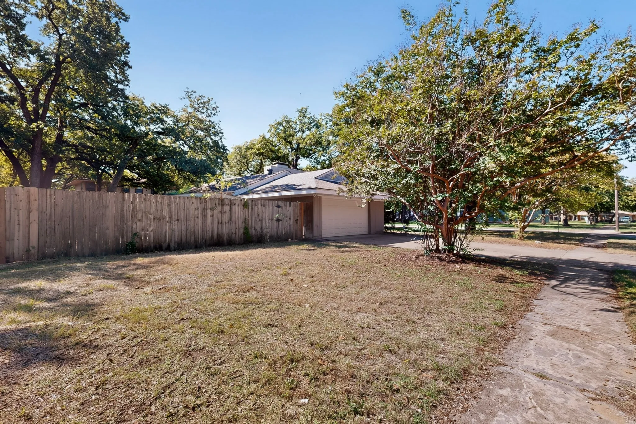 Enclosed backyard featuring a tall wooden fence, mature trees, and a concrete driveway leading to the garage