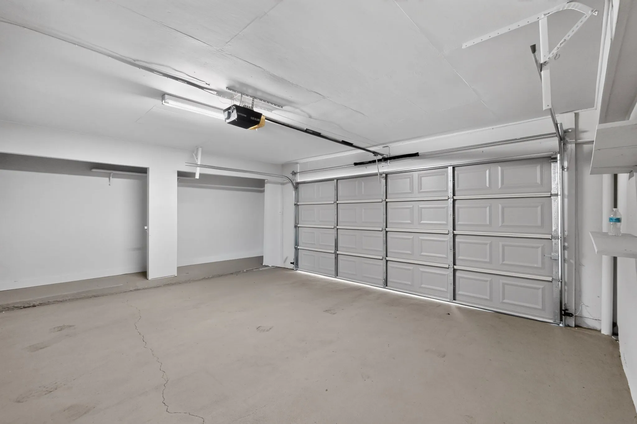 Spacious garage with an automatic overhead door, concrete flooring, and built-in shelving