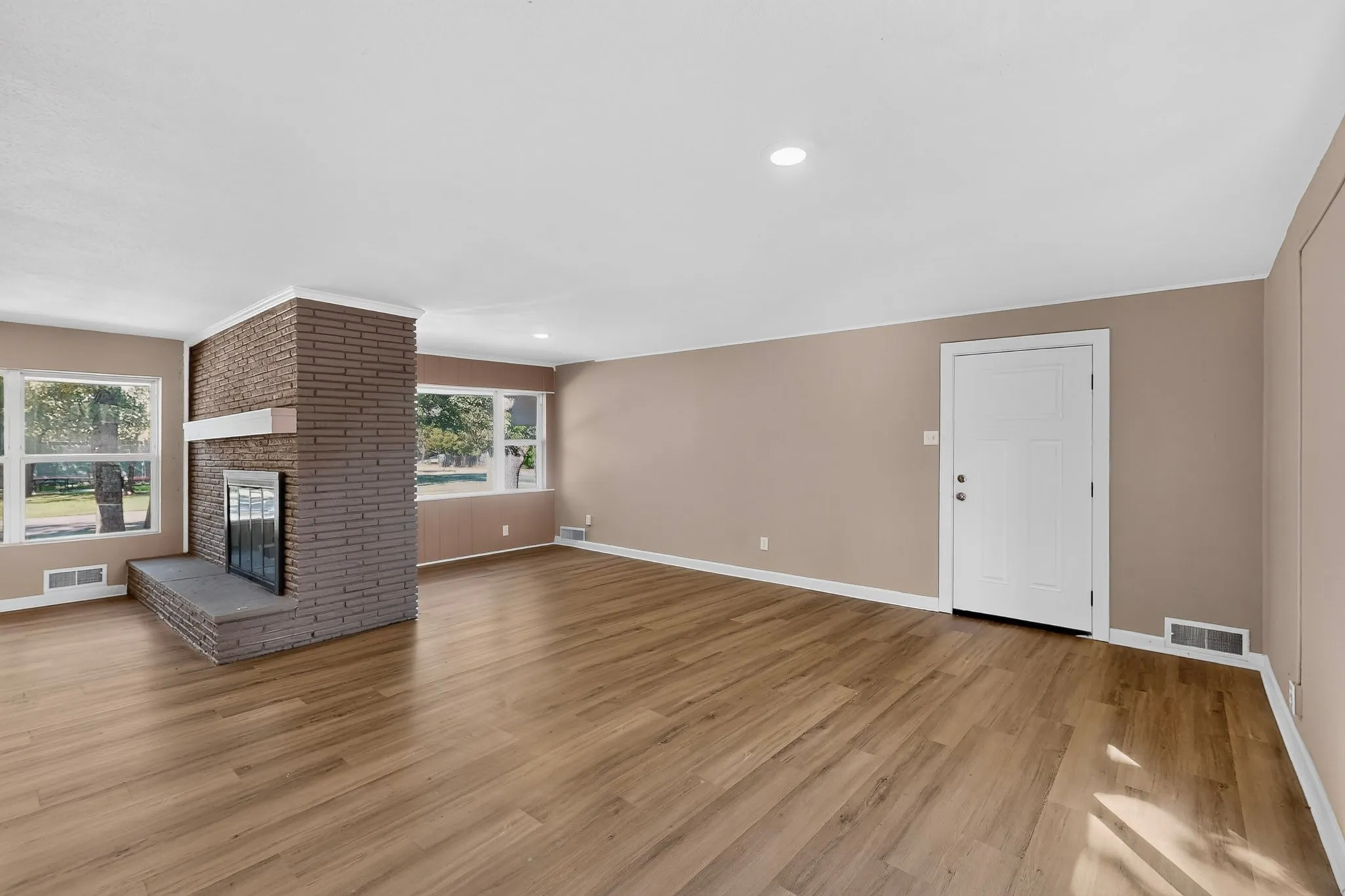 Spacious interior with wood-finish flooring, a brick fireplace with a stone hearth, recessed lighting, and multiple windows