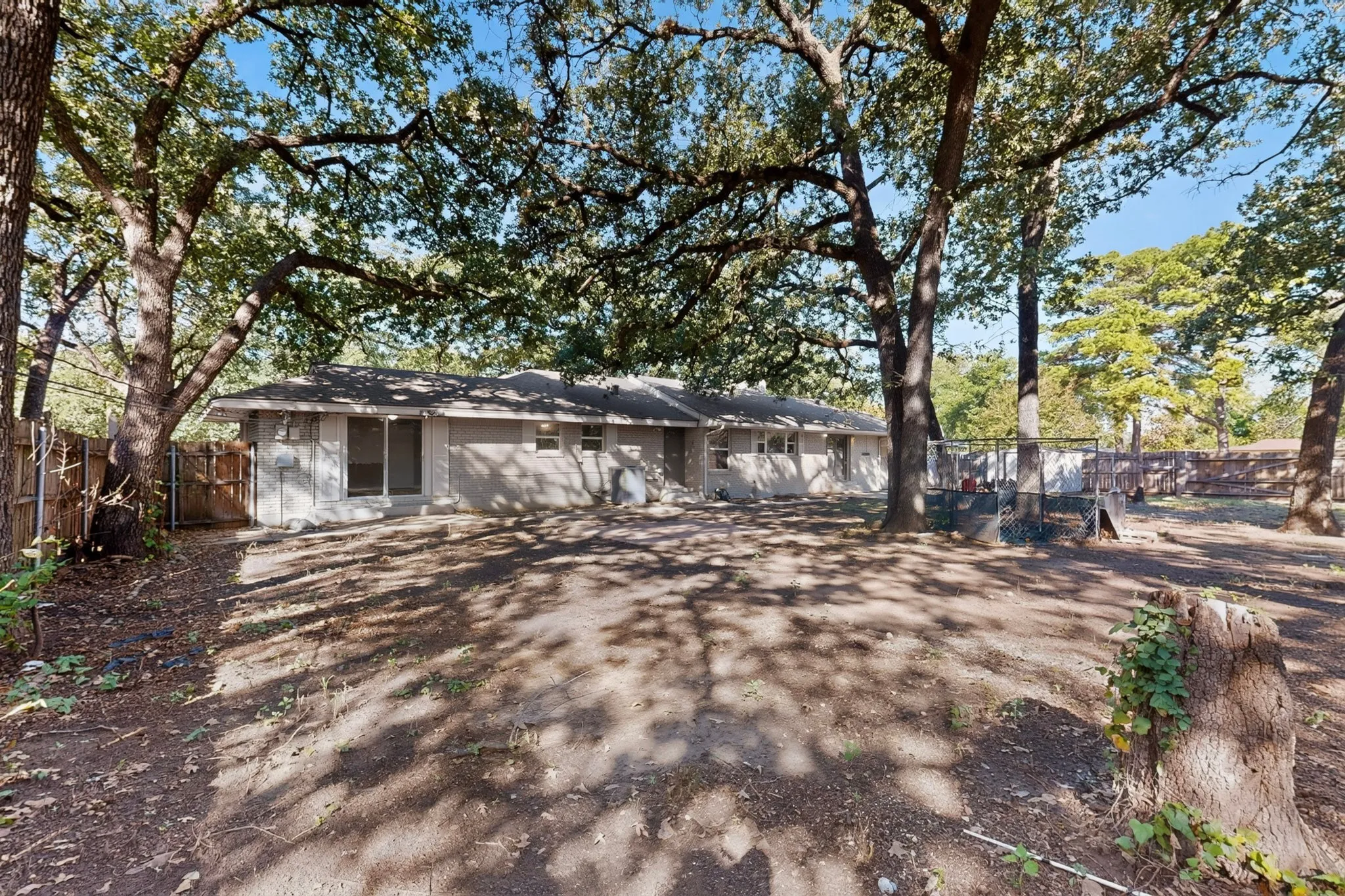 Expansive rear yard with mature trees, fenced perimeter, and a light-colored exterior with sliding glass doors
