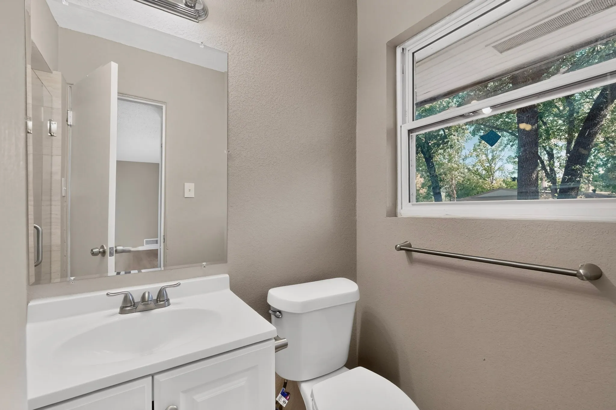 White vanity with integrated sink, brushed nickel faucet, wall-mounted mirror, and a window with natural light