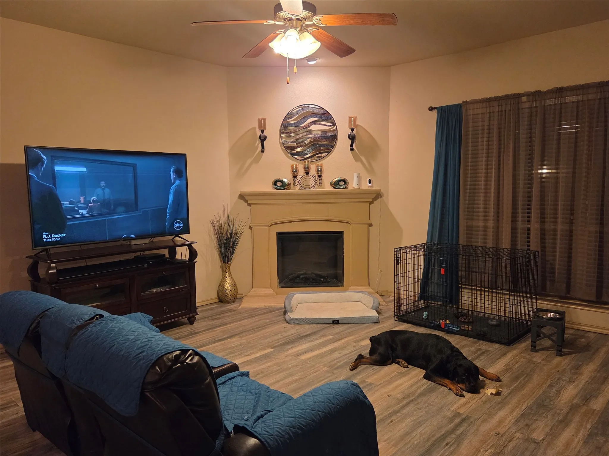 Corner fireplace with a mantel, wood-finish flooring, and ceiling fan