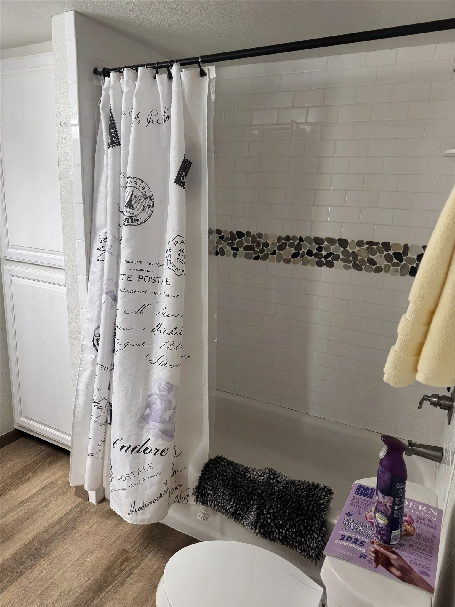 White subway tile shower surround with a decorative pebble accent band, a built-in tub, and wood-finish flooring