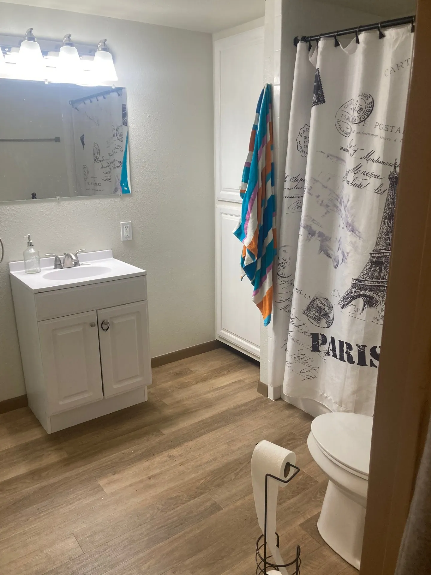 White vanity with integrated sink, wood-finish flooring, built-in storage cabinetry, and a shower with a curtain rod