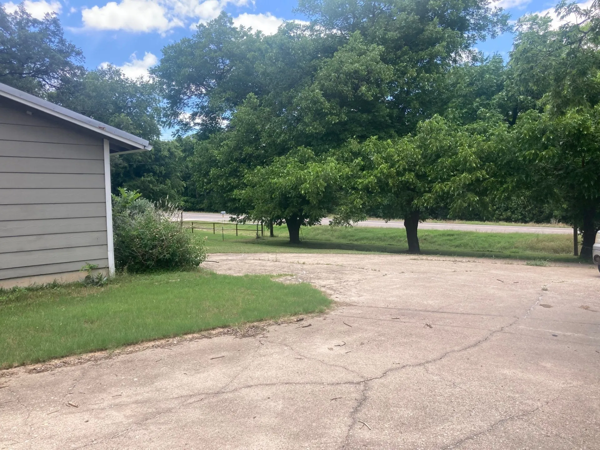 Paved drive area with surrounding mature trees and a partial exterior featuring horizontal siding