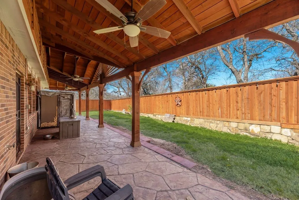 Expansive covered patio featuring a stamped concrete surface, ceiling fans, and exposed wood beam construction