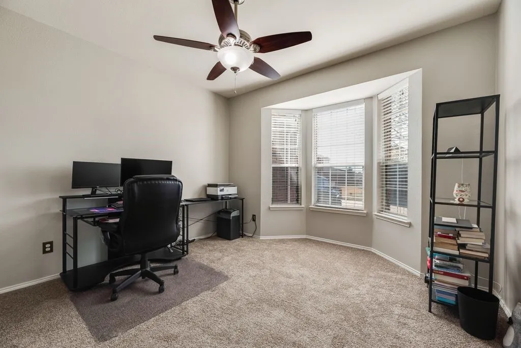 Bay window with multiple window panes, ceiling fan with light fixture, light neutral wall paint, and carpeted flooring