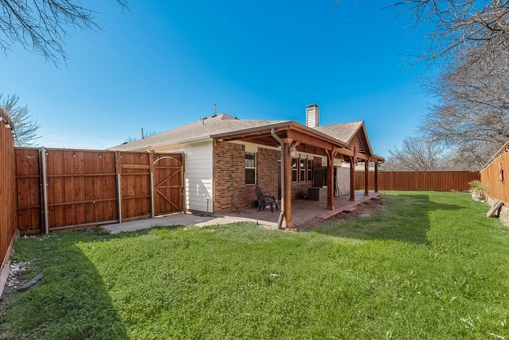 Expansive backyard featuring a covered patio, privacy fencing, and a brick exterior with white siding
