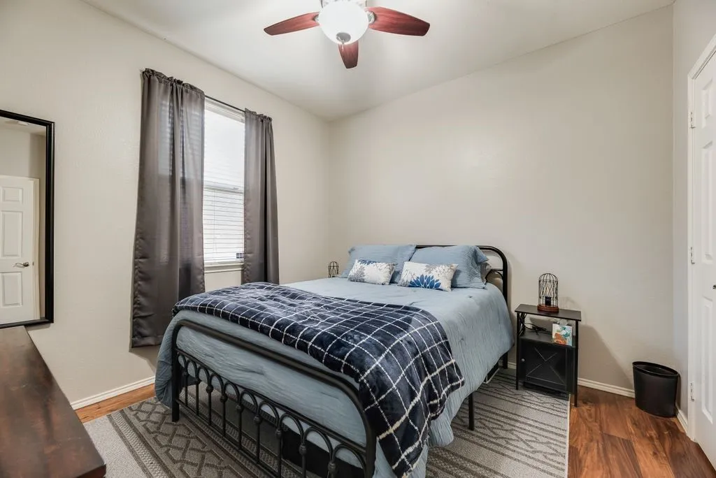 Room featuring wood-finish flooring, a ceiling fan, and a single window with blinds and drapes
