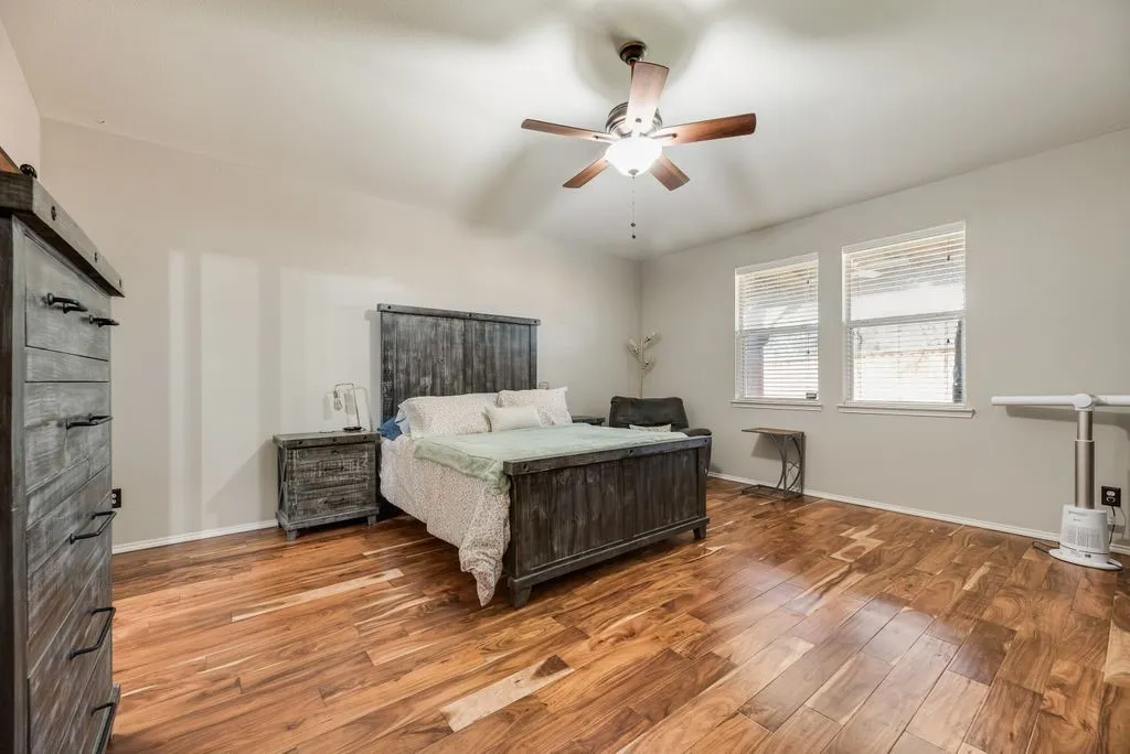 Wood-finish flooring, two large windows, vaulted ceiling, and a ceiling fan with integrated lighting