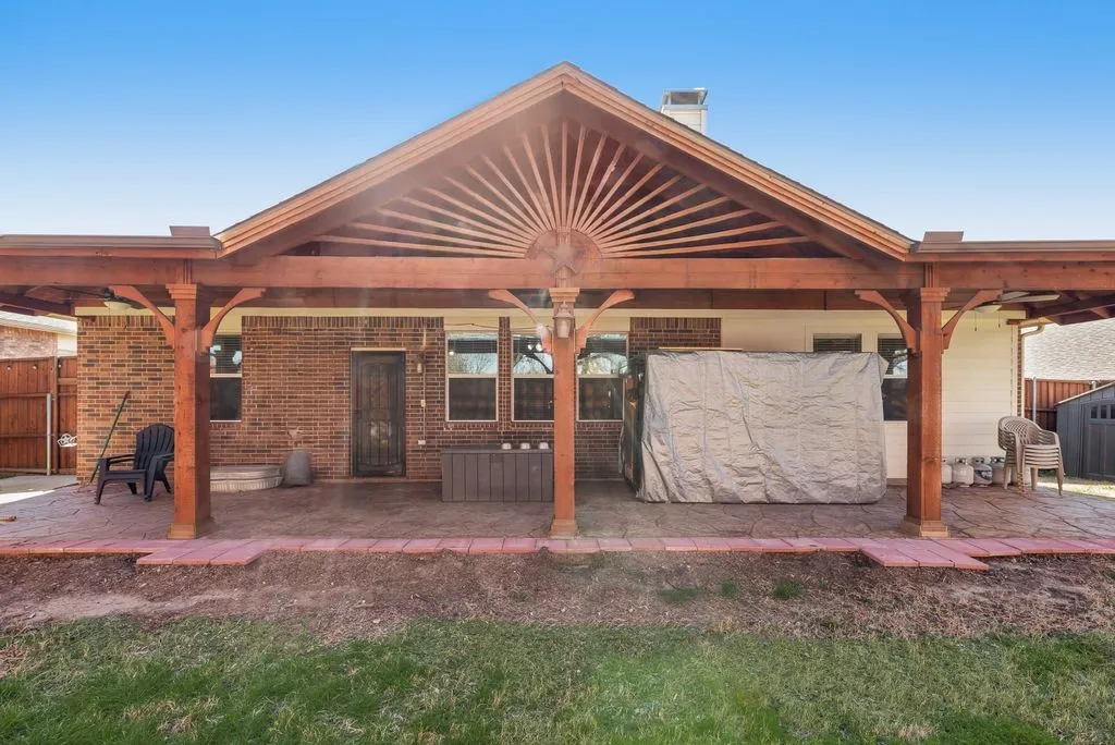 Spacious covered patio with wood-finish pergola structure, brick exterior, multiple windows, and a privacy fence