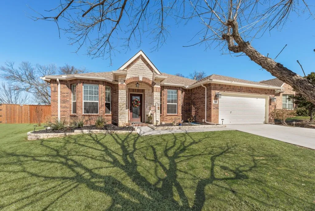 Brick and stone facade with an arched entry, two-car garage, concrete driveway, and a wood privacy fence