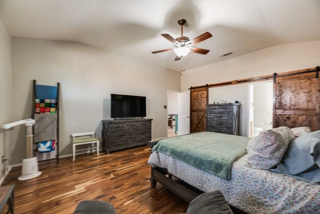 Vaulted ceiling, ceiling fan, wood-finish flooring, wood barn doors, and a white door