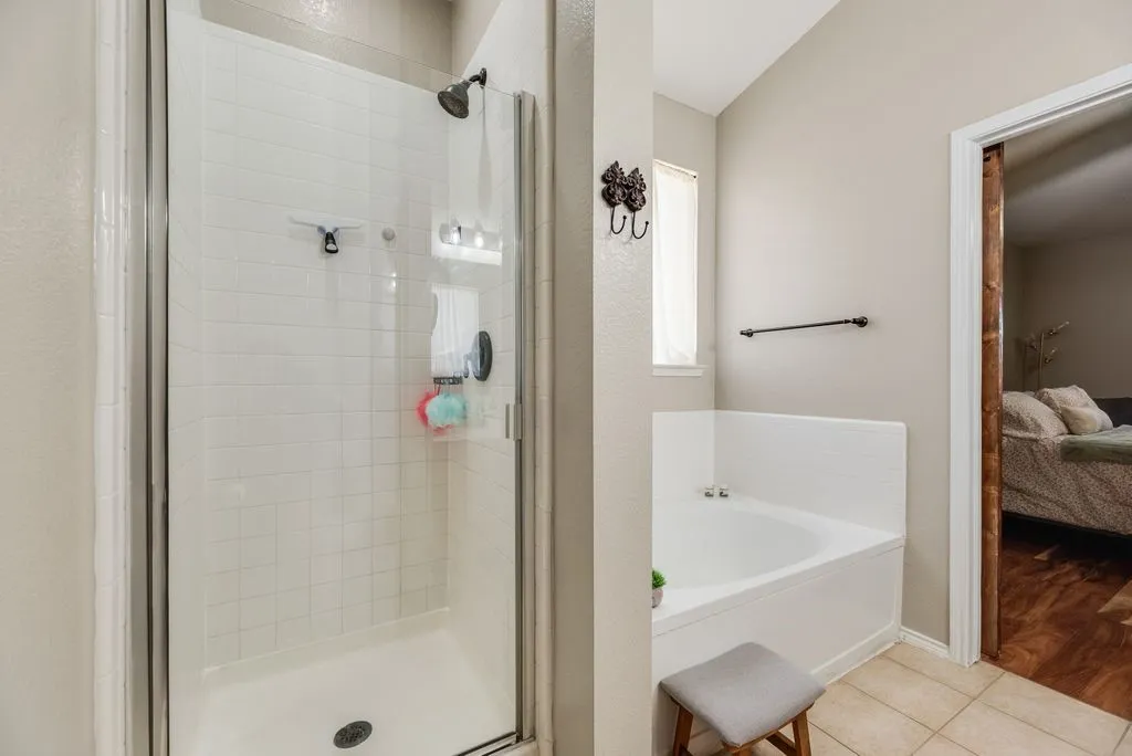 White tiled shower with glass enclosure, corner soaking tub, and neutral-toned wall paint