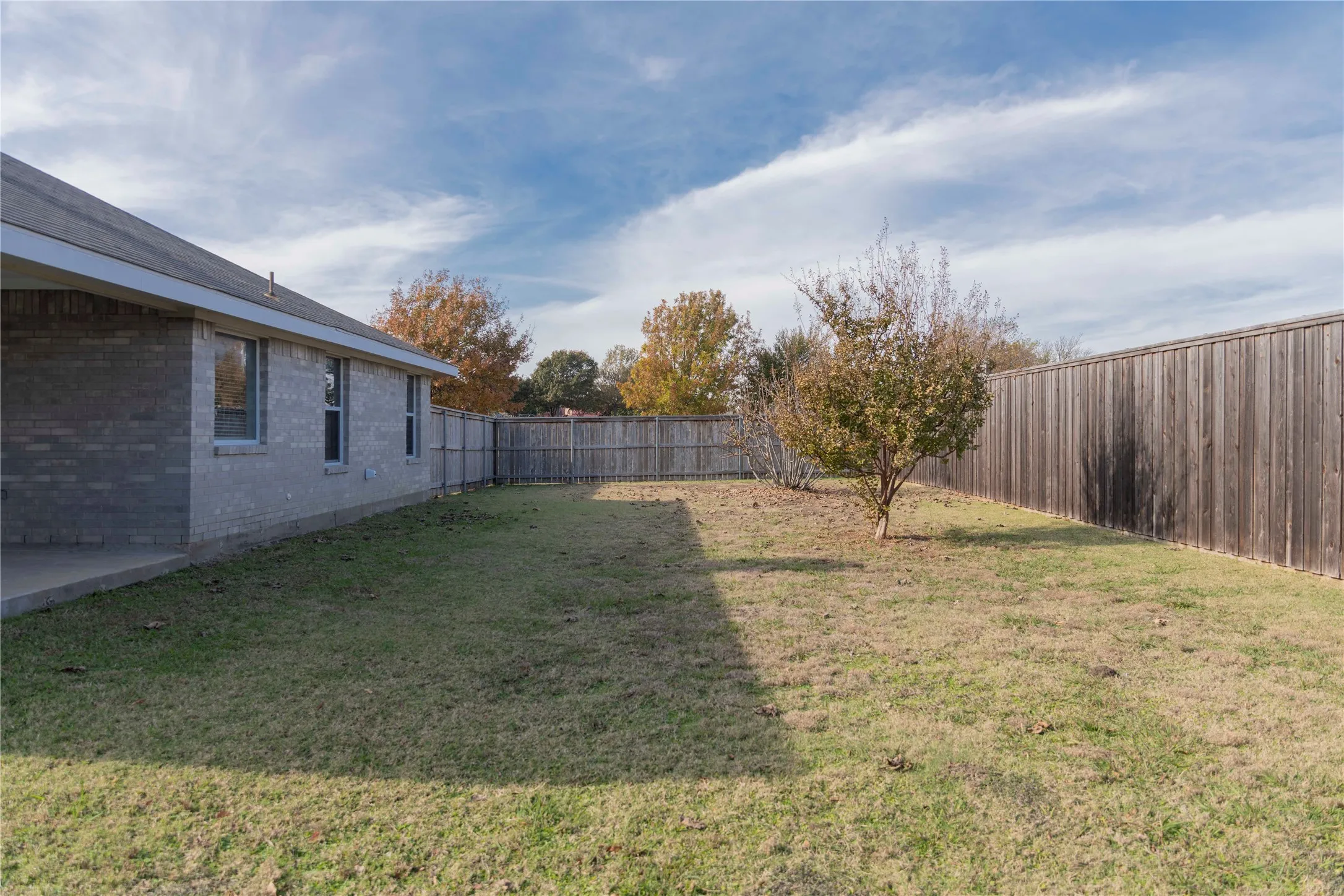Expansive grassy yard with a privacy fence, established trees, and a concrete patio